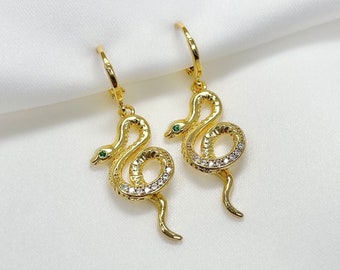 May include: A pair of gold snake earrings with clear and green gemstones. The snakes are coiled and have a dangling tail.
