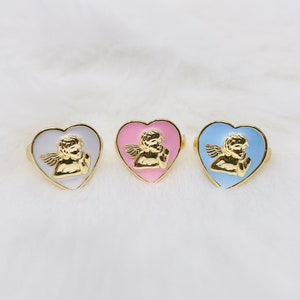Puede incluir: Tres anillos de oro en forma de coraz&oacute;n con un dise&ntilde;o de querub&iacute;n. Los anillos son de color blanco, rosa y azul claro.