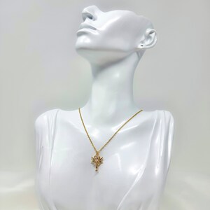 May include: A gold chain necklace with a pendant featuring a stylized key with wings. The pendant is on a white mannequin.