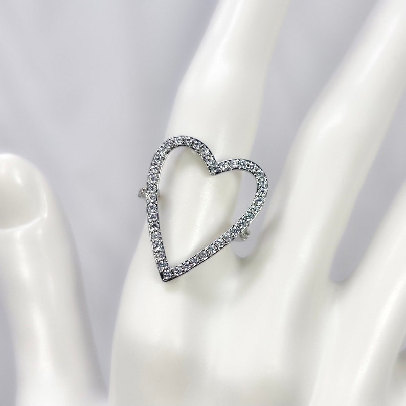 Puede incluir: Un anillo de plata con un dise&ntilde;o en forma de coraz&oacute;n. El coraz&oacute;n est&aacute; bordeado de peque&ntilde;as piedras transparentes.
