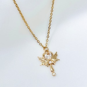 May include: A gold necklace with a heart-shaped pendant with wings. The pendant has a clear crystal in the center.