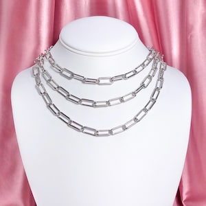 May include: Three silver chain necklaces with a rectangular link design. The necklaces are layered on a white mannequin bust.