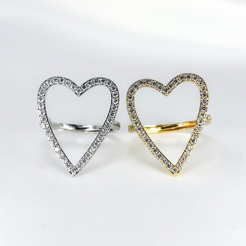 Puede incluir: Dos anillos en forma de coraz&oacute;n con un contorno de piedras transparentes. Un anillo es de plata y el otro es de oro.