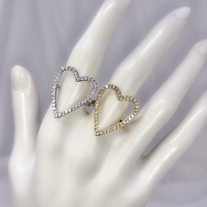 Puede incluir: Dos anillos en forma de coraz&oacute;n con un contorno de cristal transparente. Un anillo es de plata y el otro es de oro.