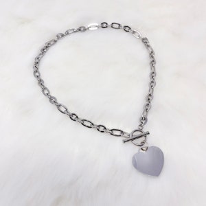 May include: A silver chain necklace with a heart-shaped pendant and a toggle clasp.