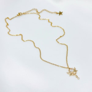 May include: A gold chain necklace with a pendant shaped like a wand with wings and a clear crystal in the center.