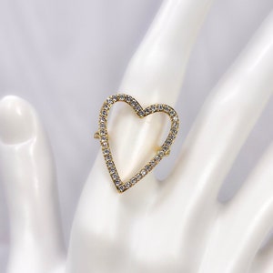 Puede incluir: Un anillo de oro en forma de coraz&oacute;n con piedras de circonita c&uacute;bica transparentes engastadas en el borde.