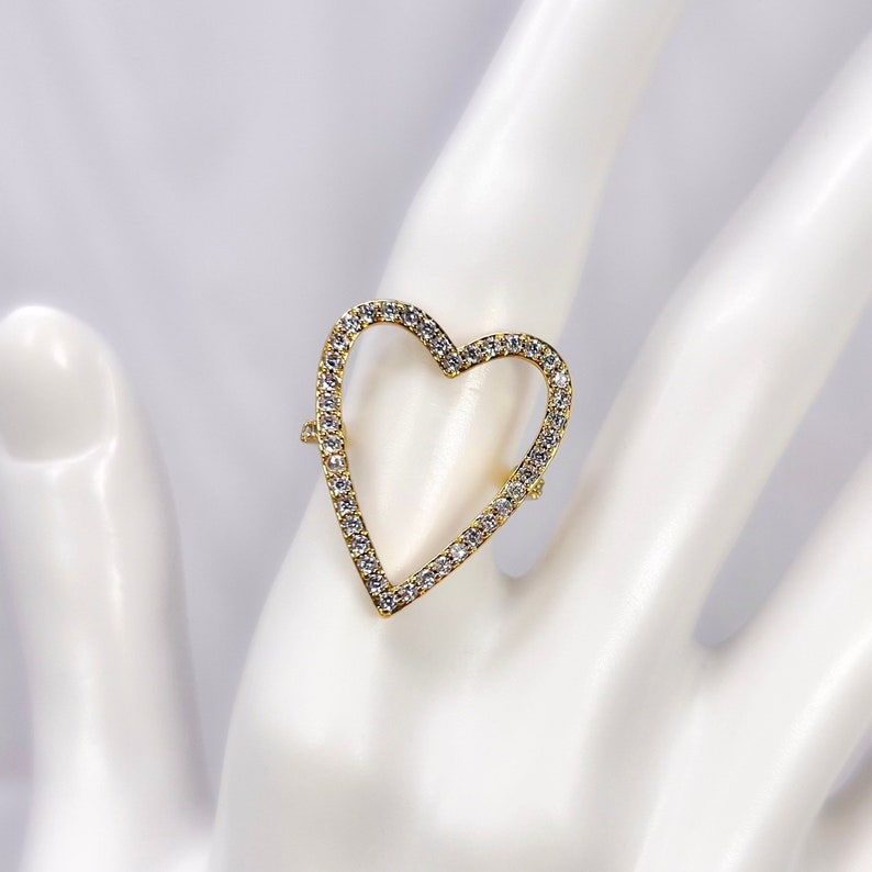Puede incluir: Un anillo de oro en forma de coraz&oacute;n con piedras de circonita c&uacute;bica transparentes engastadas en el borde.