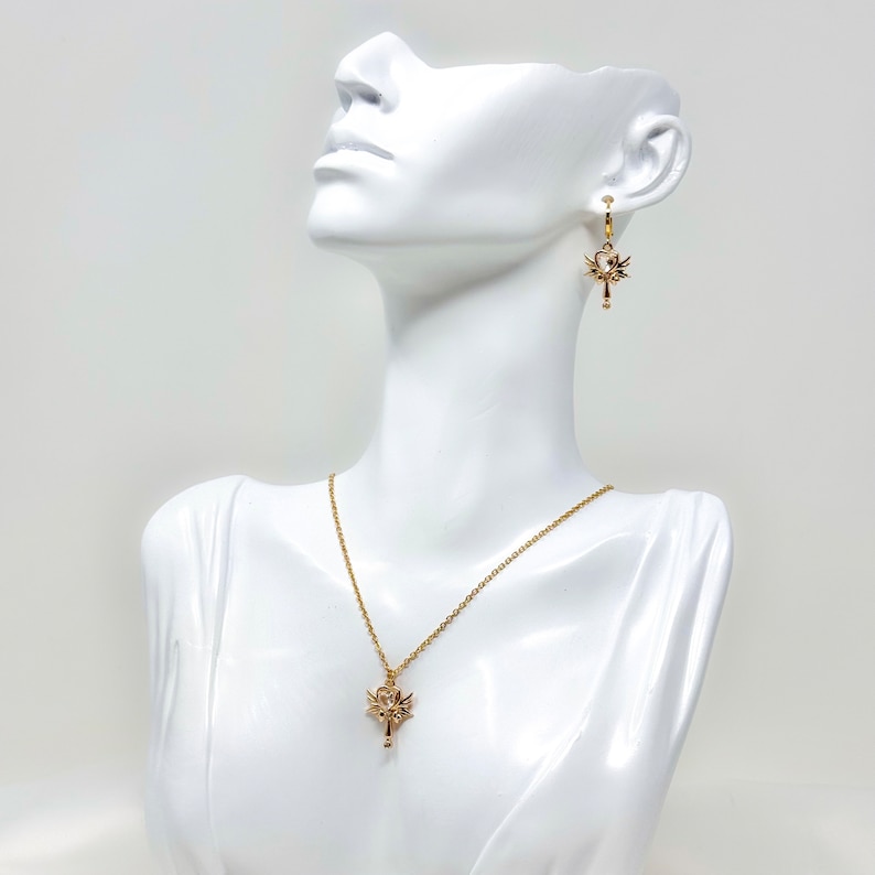 May include: A gold necklace and earrings set featuring a delicate key pendant with intricate details. The key pendant has a small, clear stone at the top.