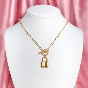 May include: A gold chain necklace with a padlock pendant and a toggle clasp.