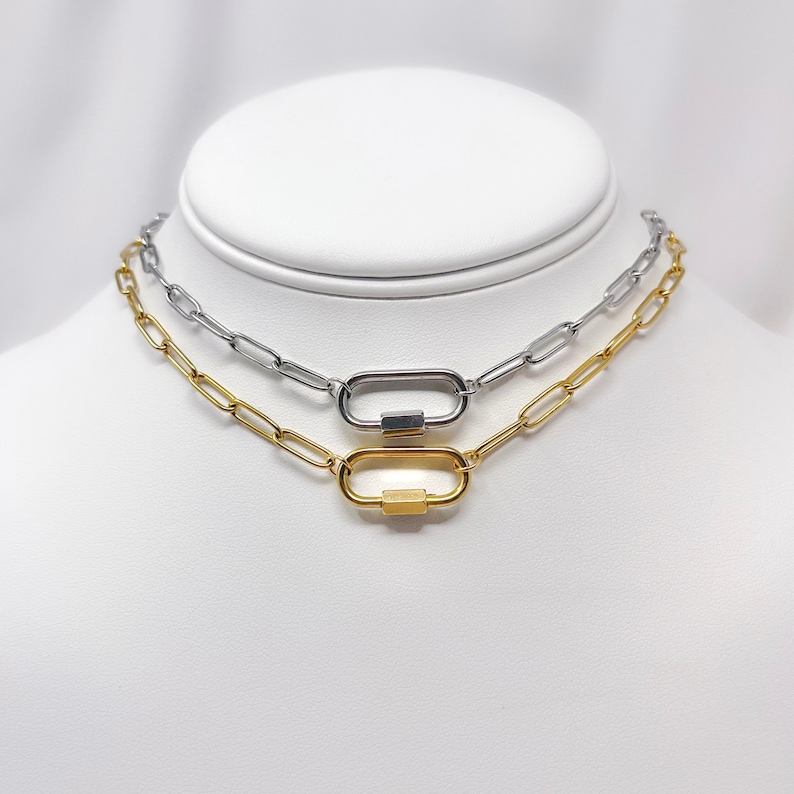 May include: Two silver and gold chain necklaces with oval-shaped clasps. The necklaces are layered on a white mannequin.