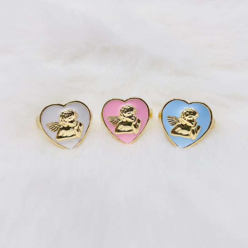 Puede incluir: Tres anillos de oro en forma de coraz&oacute;n con un dise&ntilde;o de querub&iacute;n. Los anillos son de color blanco, rosa y azul claro.