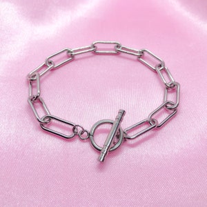 May include: A silver chain bracelet with a toggle clasp. The bracelet is made of oval-shaped links.