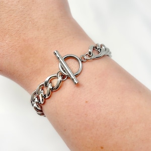 May include: A silver chain bracelet with a toggle clasp. The bracelet is made of thick, chunky links.