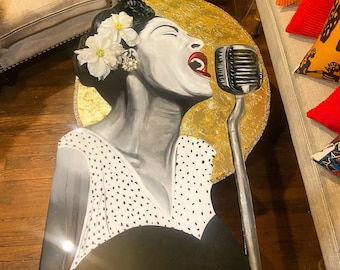 Peut inclure: Un portrait en noir et blanc d'une femme chantant dans un microphone. Le portrait est peint sur une surface ronde en feuille d'or. La femme porte une robe blanche à pois noirs et une fleur dans les cheveux.