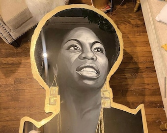 Peut inclure: Un portrait en noir et blanc d'une femme avec de grandes boucles d'oreilles dorées et un collier doré. Le portrait est peint sur un plateau de table rond en verre noir avec une bordure dorée.