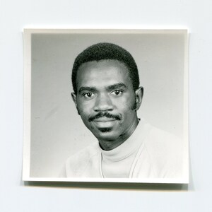 May include: A black and white photograph of a man with a mustache and goatee. He is wearing a light-colored shirt and has a serious expression on his face.