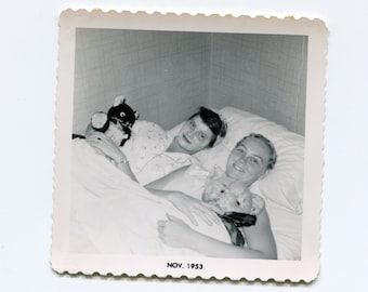 May include: Black and white photo of two women in a bed, one holding a stuffed animal. The photo is dated "NOV. 1953".