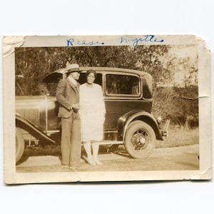 May include: Sepia-toned photograph of a man and woman posing next to a vintage black car. The man wears a suit and hat, while the woman is in a white dress. The photo is aged, with the names "Rease" and "Myrtle" written in blue ink.