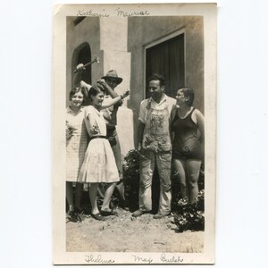 May include: A vintage black and white photograph of a group of people posing outdoors. The photo features a man in overalls, a woman in a swimsuit, and several other individuals. The names "Thelma", "May Buelah", and "Katherine Maurise" are written on the photo.