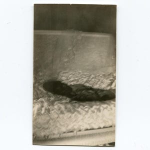 May include: A black and white vintage photograph of a person lying on a bed with a white, ruffled bedspread.