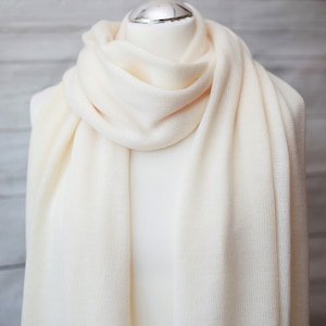 May include: A soft, white knitted scarf with a ribbed texture. The scarf is draped over a white mannequin.