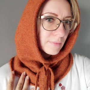 Könnte beinhalten: Ein rostiger Strickkragen mit einer langen, fließenden Krawatte. Der Kragen wird von einer Person mit blonden Haaren und Brille getragen.