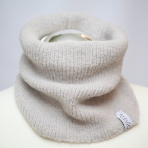 Può includere: Un collo di lana a maglia grigio chiaro con una piccola etichetta bianca che dice "ALEVICO".