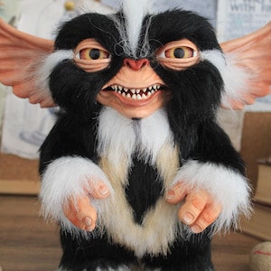 Peut inclure: Poupée Gremlin faite à la main, corps en fourrure noire et blanche, touffe de cheveux blancs et grandes oreilles. La poupée a un sourire sinistre, des yeux jaunes et une cravate noire. Objet de collection unique.