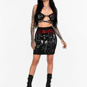 Puede incluir: Un conjunto de dos piezas negro que consta de un top bralette corto con tirantes finos y una minifalda a juego. Ambas piezas presentan un estampado gráfico en negro, blanco y rojo, con la palabra "OZZY" impresa en rojo en la parte delantera.