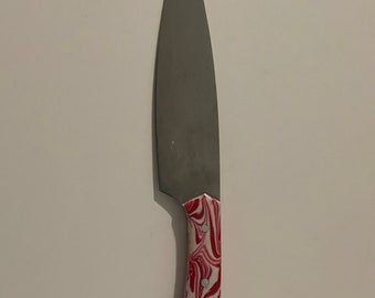 May include: A silver chef's knife with a red and white marbled handle.