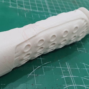 May include: White plastic handle with a textured grip and a series of small holes. The handle is part of a larger object, possibly a tool or a weapon.