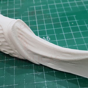 May include: White 3D printed object with a textured surface and a curved shape. The object has a series of small holes on one side.