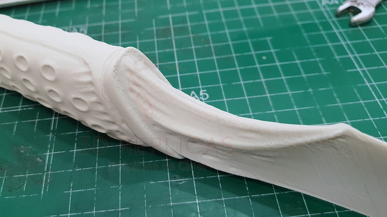 May include: White 3D printed object with a textured surface and a curved shape. The object has a series of small holes on one side.