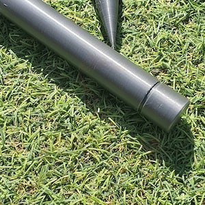 May include: Close-up of a gray metal tent pole with a rounded end cap. The pole is lying on a bed of green artificial grass.