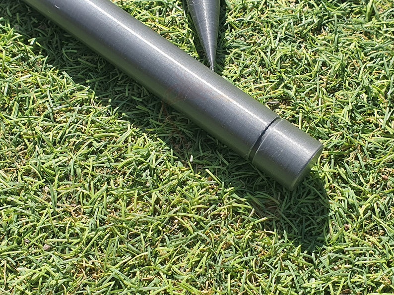 May include: Close-up of a gray metal tent pole with a rounded end cap. The pole is lying on a bed of green artificial grass.