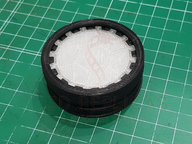 May include: A black plastic filter with a white mesh insert. The filter has a circular shape and a textured outer edge.