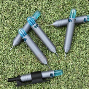May include: Six gray and blue plastic darts with a blue tip and a silver needle point. The darts are lying on a green grassy surface.
