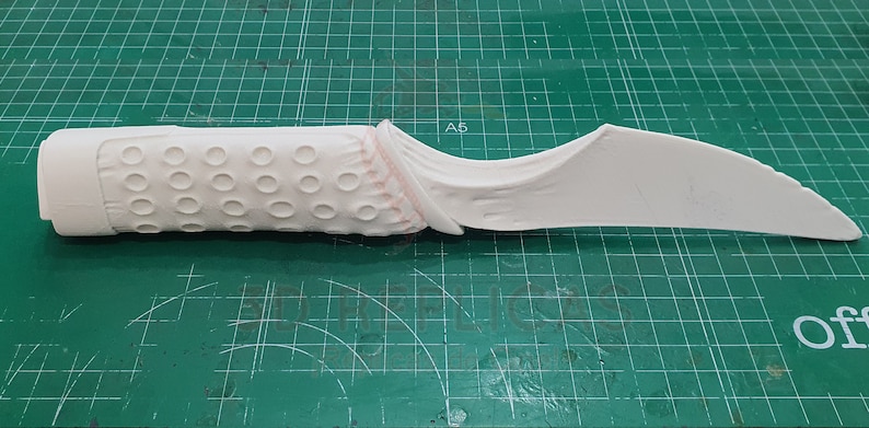 May include: White plastic prop knife with a textured handle and a curved blade. The handle has a series of small circles.
