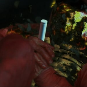 May include: A close-up of a person wearing a red jumpsuit with a glowing, green, and yellow pattern on their face. The person's face is obscured by the pattern.