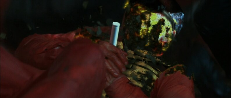 May include: A close-up of a person wearing a red jumpsuit with a glowing, green, and yellow pattern on their face. The person's face is obscured by the pattern.