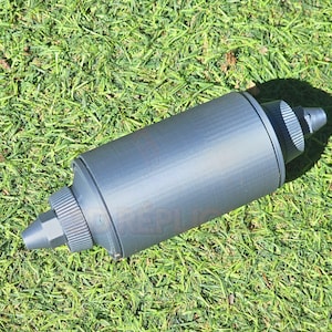 Op de afbeelding: Een grijze plastic fles met een tuit en een geribbelde textuur. De fles ligt op een bed van groen gras.