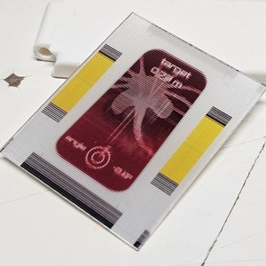 Peut inclure: Un autocollant rectangulaire blanc avec une image rouge et noire d'un palmier. L'autocollant a des rayures noires et grises et des barres jaunes sur les côtés. Le texte "target 00:00" est imprimé sur l'autocollant.