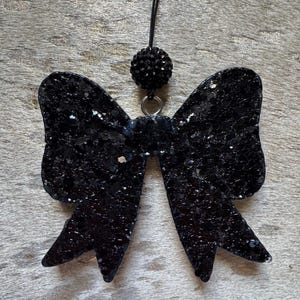 Peut inclure: Un n&oelig;ud en paillettes noires avec un accent en strass noir suspendu &agrave; une ficelle noire.