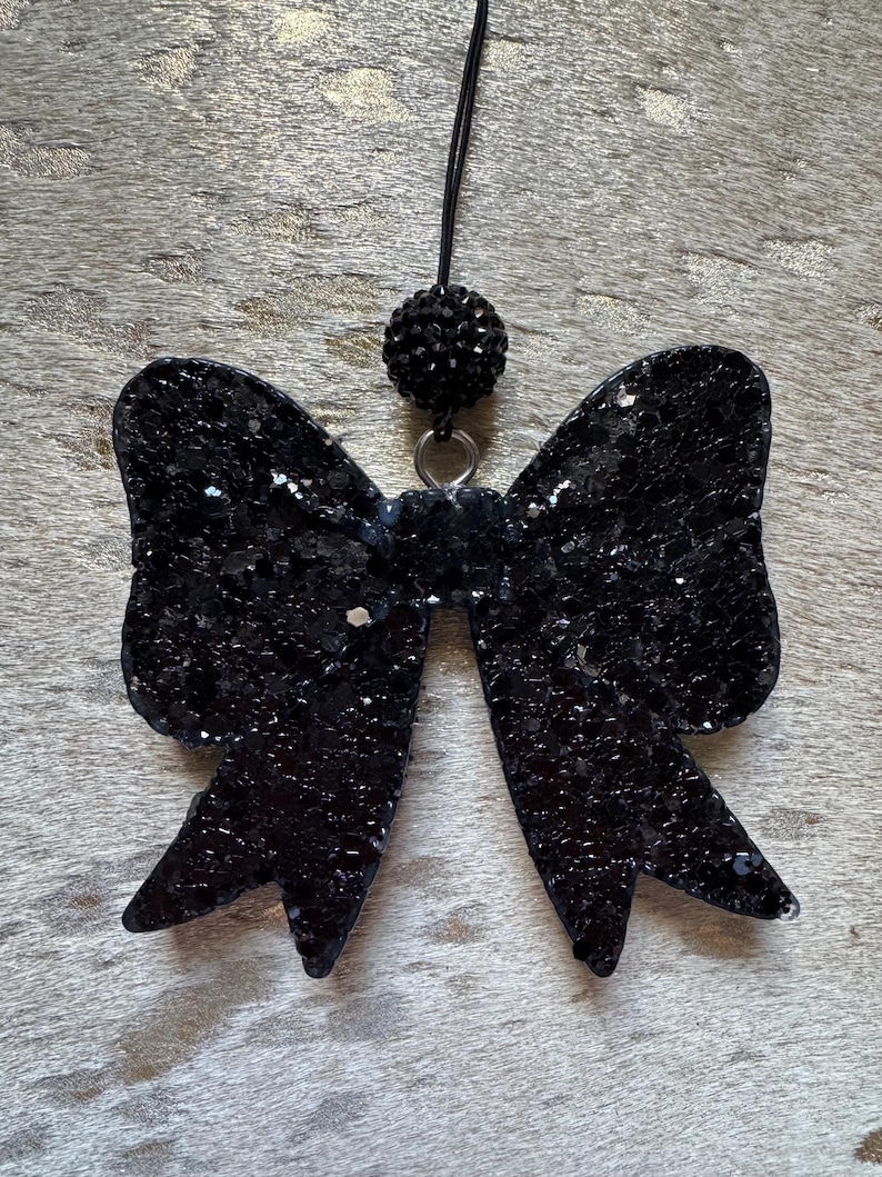 Peut inclure: Un n&oelig;ud en paillettes noires avec un accent en strass noir suspendu &agrave; une ficelle noire.