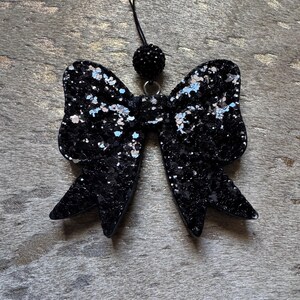 Peut inclure: Un n&oelig;ud en paillettes noires avec un pendentif noir perl&eacute; suspendu &agrave; une ficelle noire.