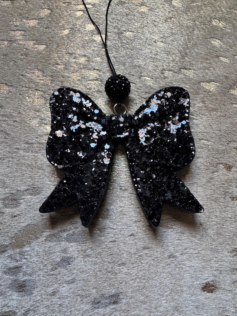Peut inclure: Un n&oelig;ud en paillettes noires avec un pendentif noir perl&eacute; suspendu &agrave; une ficelle noire.
