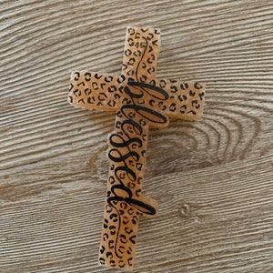 May include: A light brown cross with a leopard print design and the word "blessed" written in black cursive.