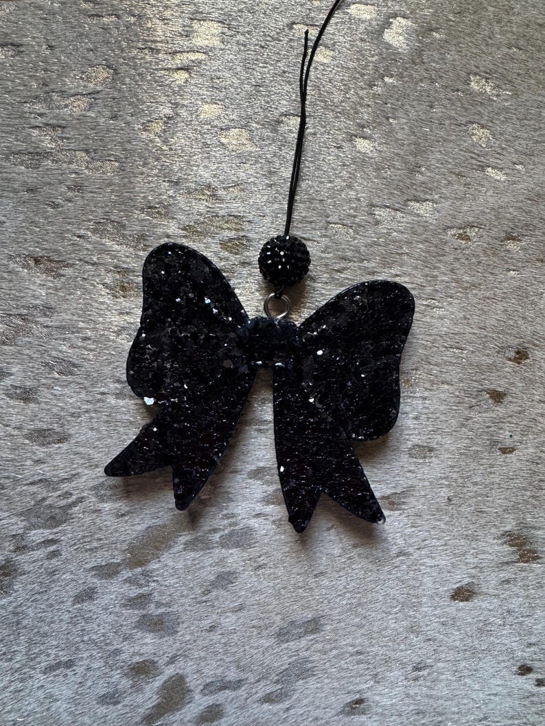 Peut inclure: Un n&oelig;ud en paillettes noires avec une perle noire au sommet, suspendu &agrave; une ficelle noire.