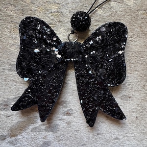 Peut inclure: Un n&oelig;ud en paillettes noires avec un accent en strass noir sur une ficelle noire.